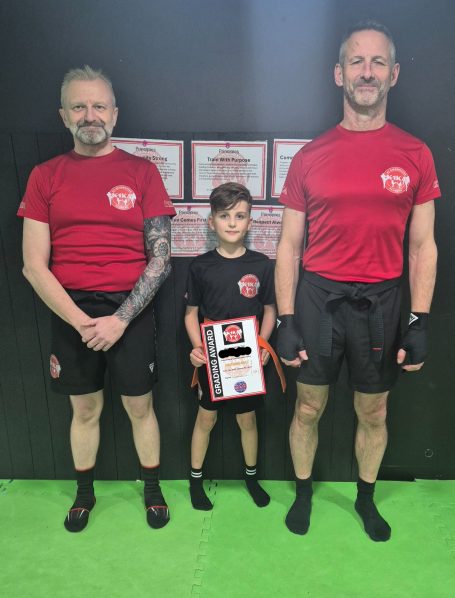 Three individuals, two adults and a child, are posing together in sports attire, holding certificates.