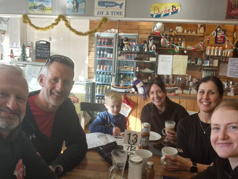 Group of six people enjoying drinks at a café, including a child. Festive decorations visible.