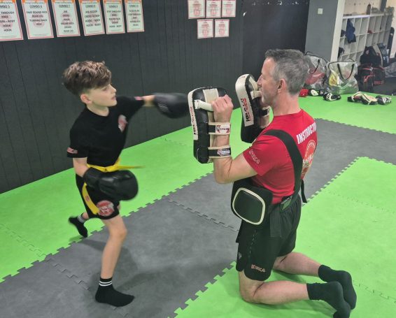 A young boy punches focus mitts held by an adult in a training gym.